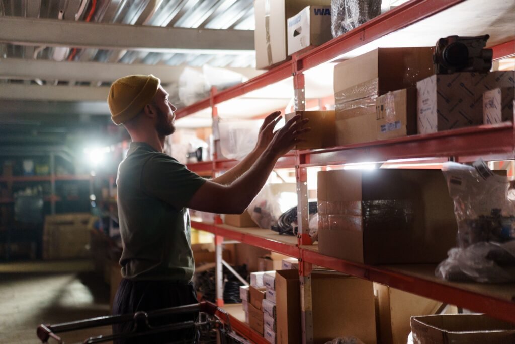 Worker organizing boxes on shelves in a warehouse, focused on logistics and storage management.